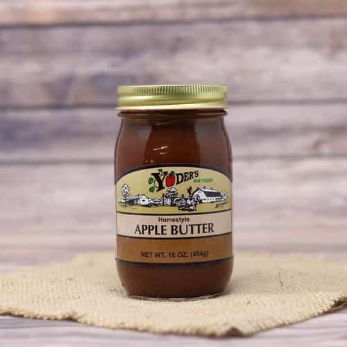 A pint size glass jar of Yoder's Fine Foods Apple Butter, on rustic burlap with a wooden background.