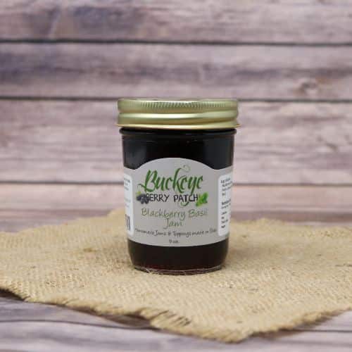 A glass jar of Buckeye Berry Patch Blackberry Basil Jam, on rustic burlap with a wooden background.
