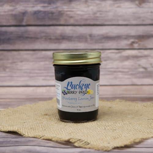 A glass jar of Buckeye Berry Patch Blueberry Lemon Jam, on rustic burlap with a wooden background.