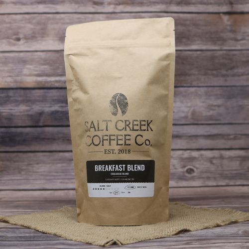 A tall brown bag of Breakfast Blend Salt Creek Coffee on rustic burlap with a wooden background.
