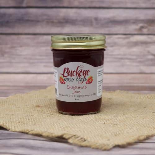 A glass jar of Buckeye Berry Patch Christmas Jam, on rustic burlap with a wooden background.