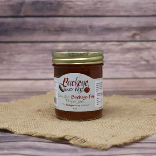 A glass jar of Buckeye Berry Patch Daudy's Buckeye Fire Pepper Jam, on rustic burlap with a wooden background.