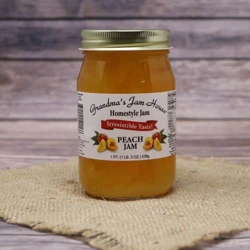 A pint size glass jar of Grandma's Jam House Peach Jam, on rustic burlap with a wooden background.