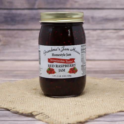 A pint size glass jar of Grandma's Jam House Red Raspberry Jam, on rustic burlap with a wooden background.
