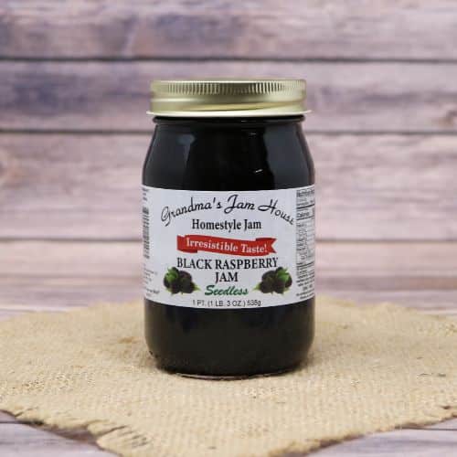 A pint size glass jar of Grandma's Jam House Seedless Black Raspberry Jam, on rustic burlap with a wooden background.