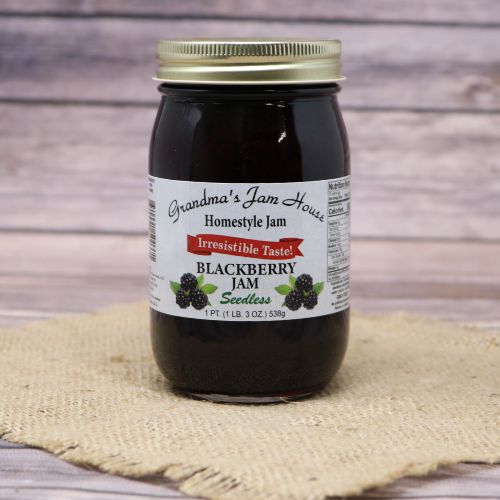 A pint size glass jar of Grandma's Jam House Seedless Blackberry Jam, on rustic burlap with a wooden background.
