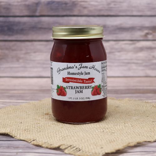 A pint size glass jar of Grandma's Jam House Strawberry Jam, on rustic burlap with a wooden background.