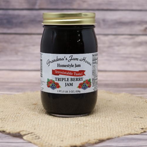 A pint size glass jar of Grandmas Jam House Triple Berry Jam, on rustic burlap with a wooden background.