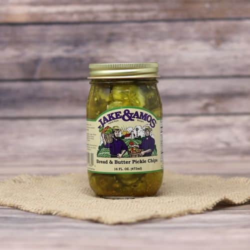 A pint size glass jar of Jake & Amos Bread & Butter Pickle Chips, on rustic burlap with a wooden background.