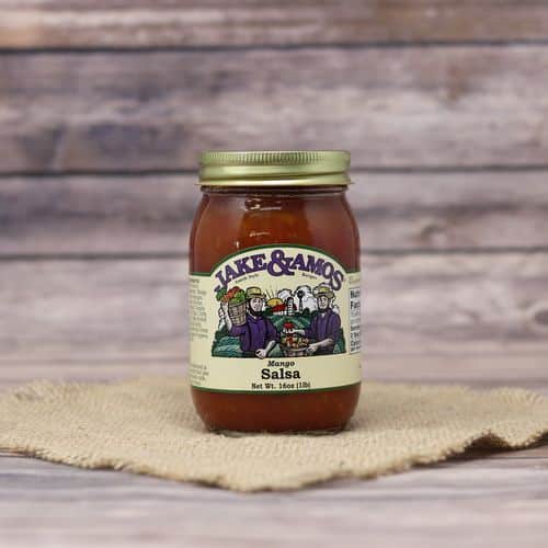 A pint size glass jar of Jake & Amos Mango Salsa, on rustic burlap with a wooden background.