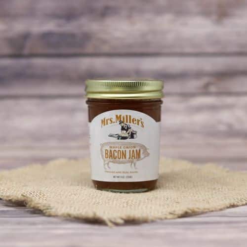 A glass jar of Mrs. Miller's Maple Onion Bacon Jam, on rustic burlap with a wooden background.