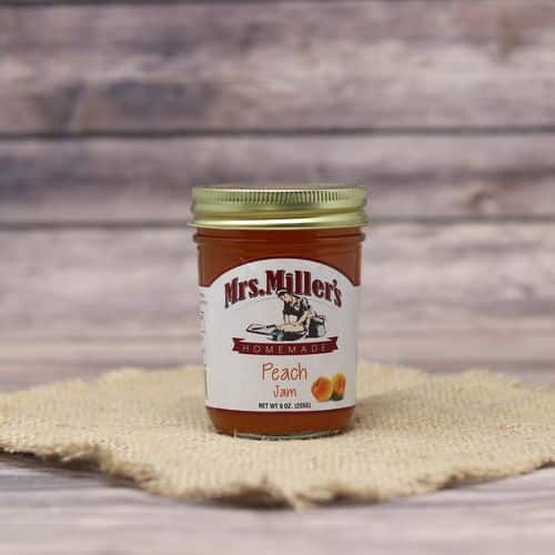 A 9oz glass jar of Mrs. Miller's Peach Jam, on rustic burlap with a wooden background.