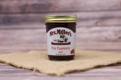 A 9 oz glass jar of Mrs. Miller's Red Raspberry Jam, on rustic burlap with a wooden background.