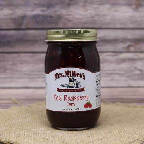 A 20 oz glass jar of Mrs. Miller's Red Raspberry Jam, on rustic burlap with a wooden background.