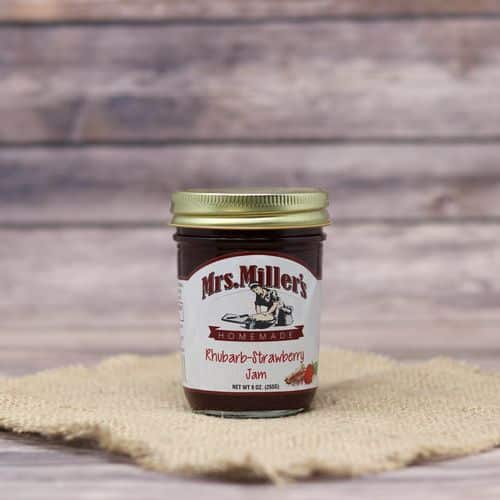 A 9oz glass jar of Mrs. Miller's Rhubarb Strawberry Jam, on rustic burlap with a wooden background.