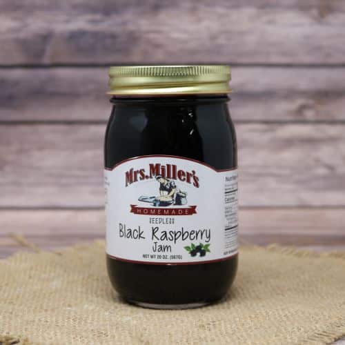 A 20 oz glass jar of Mrs. Miller's Seedless Black Raspberry Jam, on rustic burlap with a wooden background.