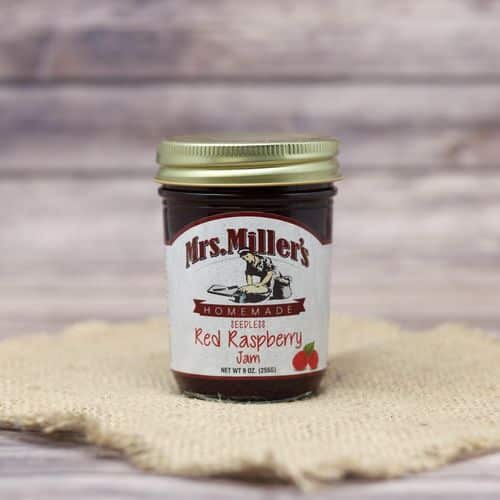A 9oz glass jar of Mrs. Miller's Seedless Red Raspberry Jam, on rustic burlap with a wooden background.