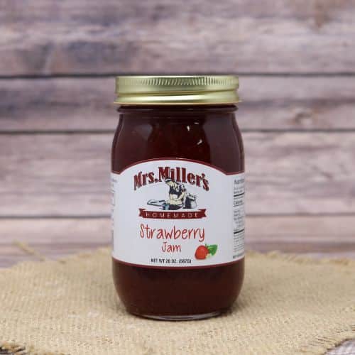 A 20 oz glass jar of Mrs. Miller's Strawberry Jam, on rustic burlap with a wooden background.