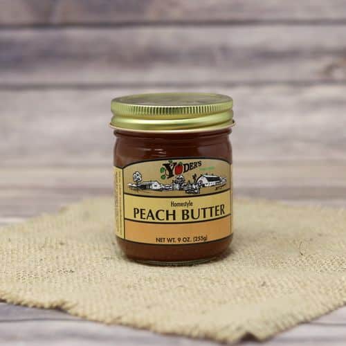 A 9 oz glass jar of Yoder's Fine Foods Peach Butter, on rustic burlap with a wooden background.