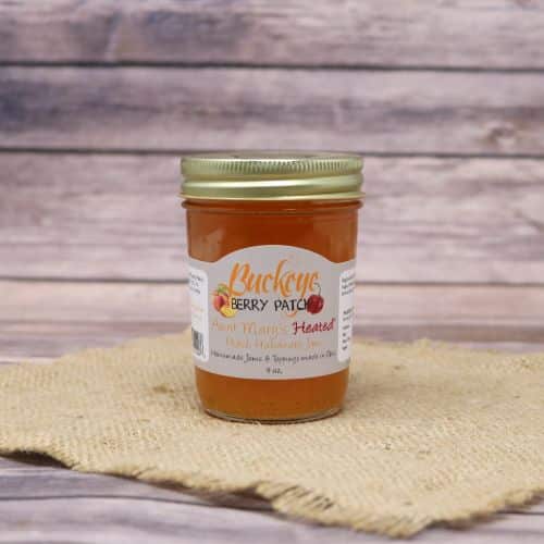 A glass jar of Buckeye Berry Patch Heated Peach Habanero Jam, on rustic burlap with a wooden background.