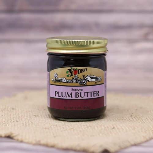 A 9 oz glass jar of Yoder's Fine Foods Plum Butter, on rustic burlap with a wooden background.