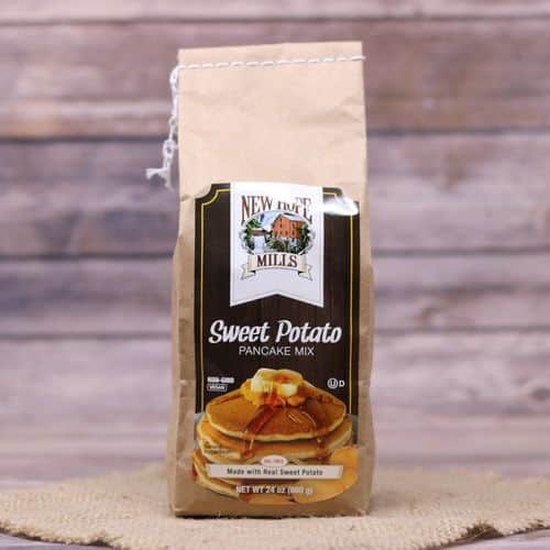 A brown bag with a dark brown label of Sweet Potato Pancake Mix on rustic burlap with a wooden background.