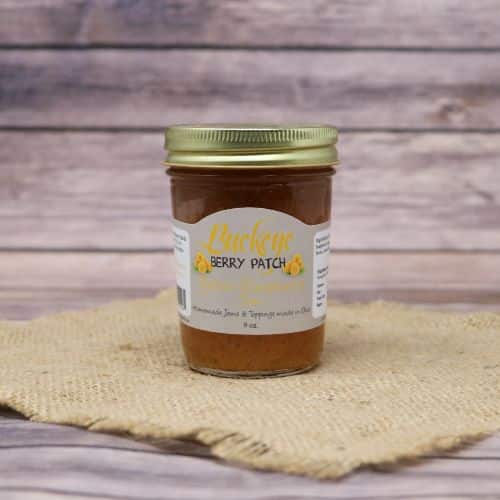 A glass jar of Buckeye Berry Patch Yellow Raspberry Jam, on rustic burlap with a wooden background.