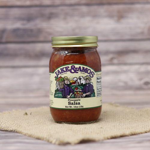 A pint size glass jar of Jake & Amos Pineapple Salsa, on rustic burlap with a wooden background.