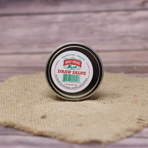 A metal container of Amish Origins Draw Salve, set on rustic burlap with a wooden background.