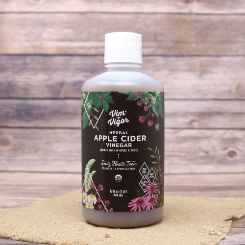 A 32 oz size bottle of Vim & Vigor Herbal Apple Cider Vinegar, set on rustic burlap with a wooden background.