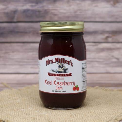 A 20 oz glass jar of Mrs. Miller's Seedless Red Raspberry Jam, on rustic burlap with a wooden background.