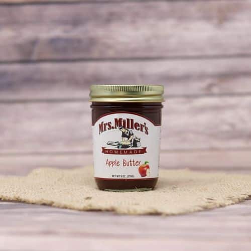 A 9 oz glass jar of Mrs. Miller's Apple Butter, on rustic burlap with a wooden background.