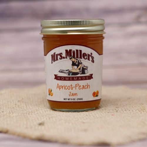 A 9 oz glass jar of Mrs. Miller's Apricot Peach Jam, on rustic burlap with a wooden background.