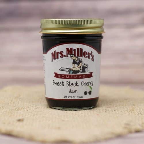 A 9 oz glass jar of Mrs. Miller's Black Cherry Jam, on rustic burlap with a wooden background.