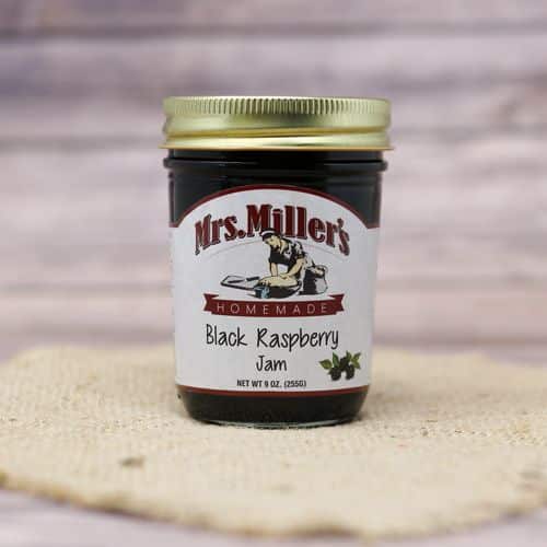 A 9 oz glass jar of Mrs. Miller's Black Raspberry Jam, on rustic burlap with a wooden background.