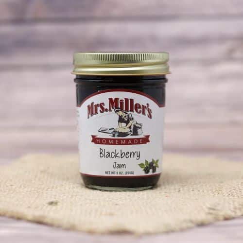 A 9 oz glass jar of Mrs. Miller's Blackberry Jam, on rustic burlap with a wooden background.