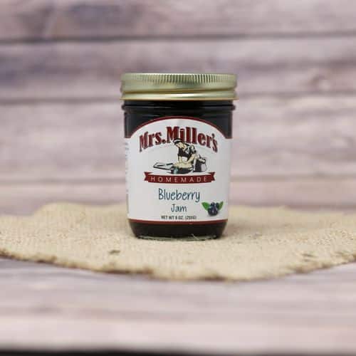 A 9 oz glass jar of Mrs. Miller's Blueberry Jam, on rustic burlap with a wooden background.