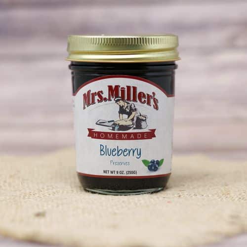 A 9 oz glass jar of Mrs. Miller's Blueberry Preserves, on rustic burlap with a wooden background.