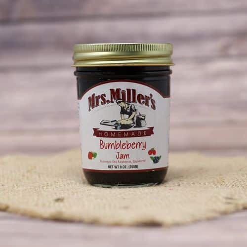 A 9 oz glass jar of Mrs. Miller's Bumbleberry Jam, on rustic burlap with a wooden background.