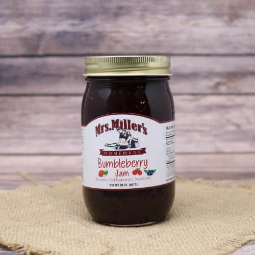 A 20 oz glass jar of Mrs. Miller's Bumbleberry Jam, on rustic burlap with a wooden background.
