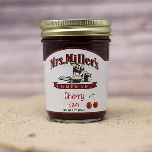 A 9 oz glass jar of Mrs. Miller's Cherry Jam, on rustic burlap with a wooden background.