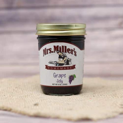 A 9 oz glass jar of Mrs. Miller's Grape Jelly, on rustic burlap with a wooden background.