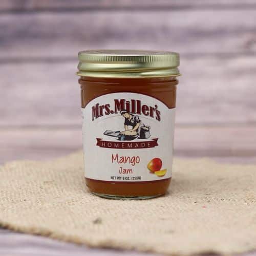 A 9 oz glass jar of Mrs. Miller's Mango Jam, on rustic burlap with a wooden background.