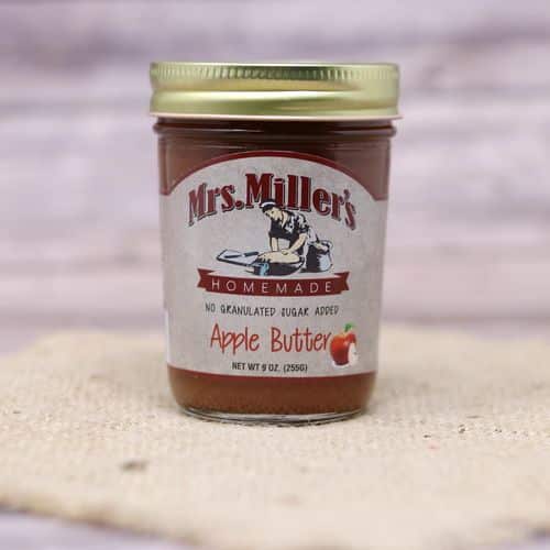 A 9 oz glass jar of Mrs. Miller's No Sugar Added Apple Butter, on rustic burlap with a wooden background.