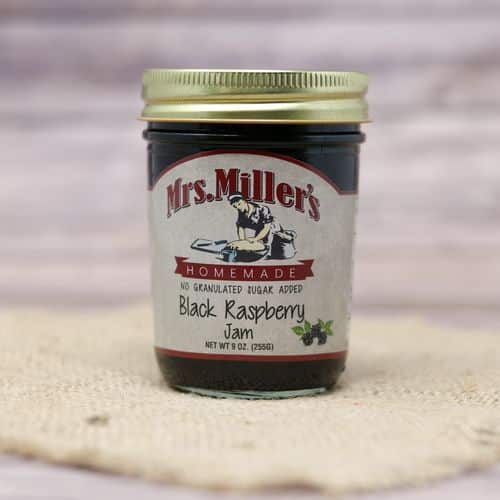 A 9 oz glass jar of Mrs. Miller's No Sugar Added Black Raspberry Jam, on rustic burlap with a wooden background.