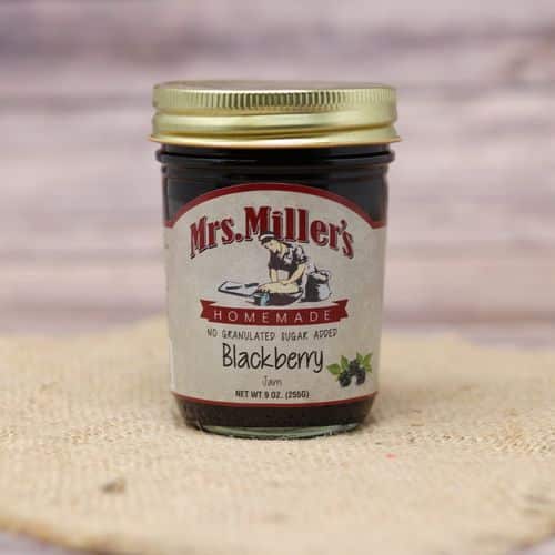 A 9 oz glass jar of Mrs. Miller's No Sugar Added Blackberry Jam, on rustic burlap with a wooden background.