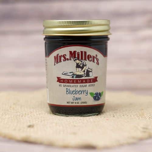 A 9 oz glass jar of Mrs. Miller's No Sugar Added Blueberry Jam, on rustic burlap with a wooden background.