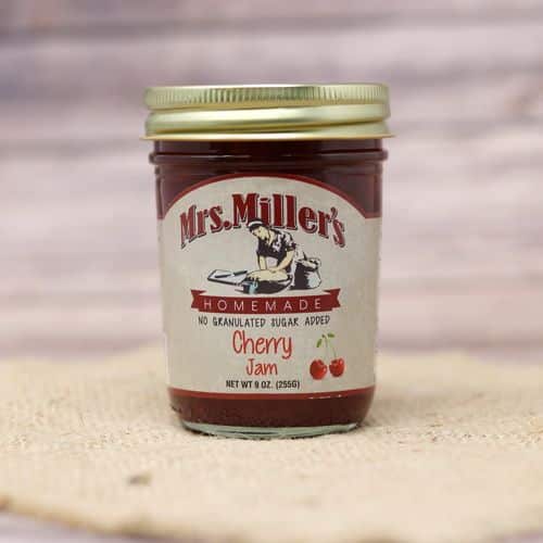 A 9 oz glass jar of Mrs. Miller's No Sugar Added Cherry Jam, on rustic burlap with a wooden background.