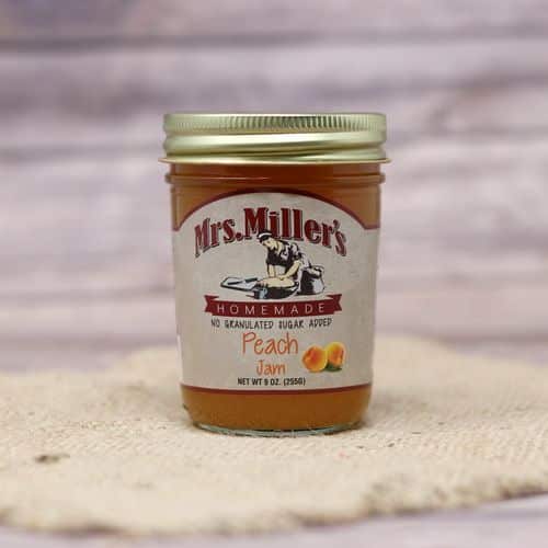 A 9 oz glass jar of Mrs. Miller's No Sugar Added Peach Jam, on rustic burlap with a wooden background.