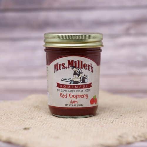 A 9 oz glass jar of Mrs. Miller's No Sugar Added Red Raspberry Jam, on rustic burlap with a wooden background.